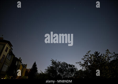 Stars over the outskirts of Vienna, Austria. Typical suburban houses and garden trees under a cloudless night sky influenced by light pollution. Stock Photo