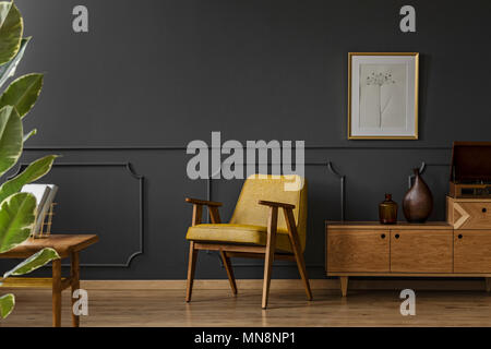 A spacious, vintage living room interior with black walls, wooden floor, yellow chair, poster and plant Stock Photo
