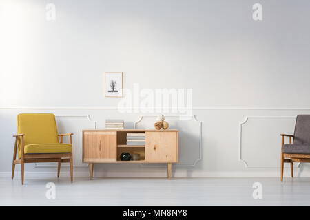 Yellow vintage armchair next to wooden cupboard against white wall in living room interior Stock Photo