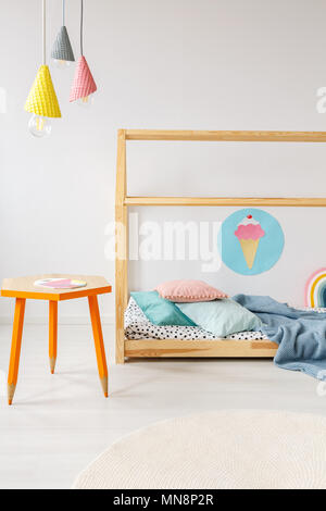 Orange table under colorful lamps in modern child's bedroom interior with wooden bed