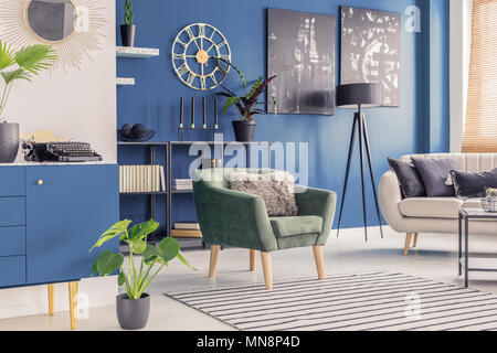 Retro typewriter and golden wall clock in a blue living room interior with paintings and modern furniture