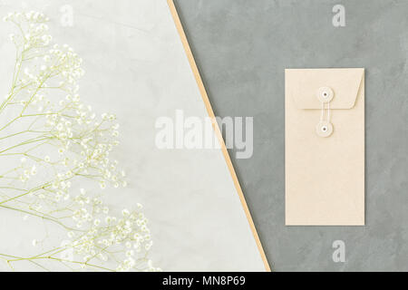 A minimalist geometrical arrangement with small white flowers and an envelope on light and dark gray backgrounds Stock Photo