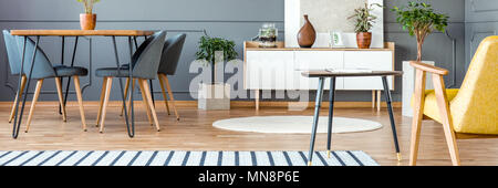 White wooden cupboard with decor and painting placed in grey dining room interior with fresh plants and hairpin table Stock Photo