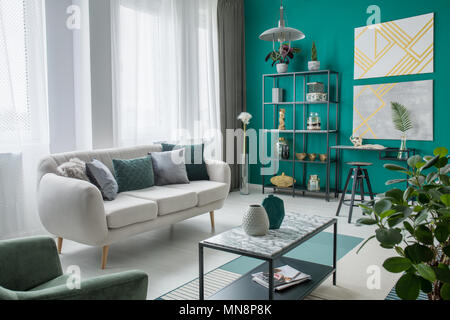 Beige sofa in cozy living room interior with gold paintings on green wall with black stool at desk Stock Photo