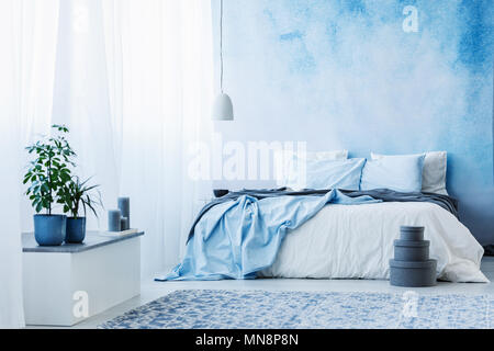 Sky blue bedroom interior with double bed, plants and grey boxes on the floor Stock Photo