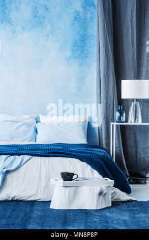 Blue watercolor paint on the wall in modern bedroom interior with a double bed and grey curtain Stock Photo