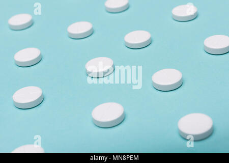 White pills on blue pastel coloured background. Medication and prescription pills background. Stock Photo