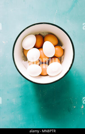 White and brown eggs in   a metallic bowl over a blue   background Stock Photo