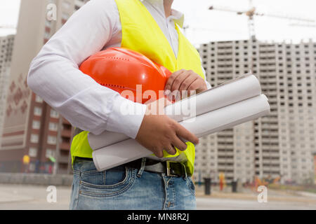 Closeup image of male builder holding blueprints and red helmet Stock Photo