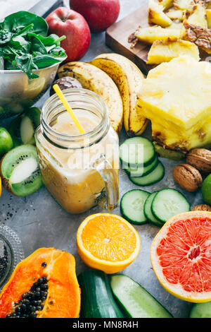 Healthy mango detox  smoothie drink in a glass surrounded by raw fruit ingredients,banana,ananas, papaya,cucumber, kale,spinach, Stock Photo