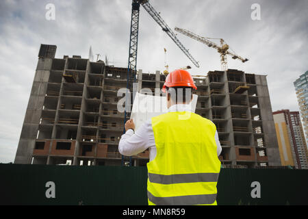 Rear view image of construction engineer checking blueprint of new building under construction Stock Photo