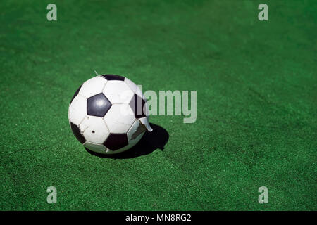 Old, dirty tattered soccer ball on background of green grass. Traditional classic black and white football ball on green field of the stadium training Stock Photo