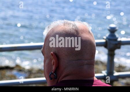 Middle aged man with punk hair and shaved head looking out to sea with blurred background Stock Photo