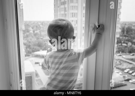 Black and white image of baby pulling window handle and trying to open it Stock Photo