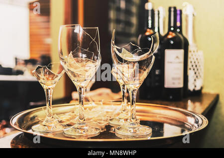 Broken wine glass on a tray with some wine and champagne bottles blurred on the background. Broken glass of a party or celebration. Stock Photo