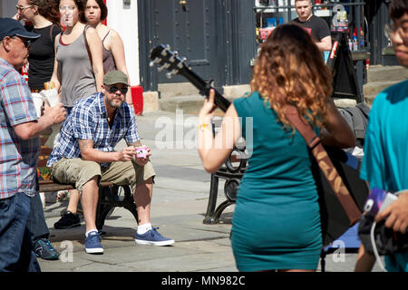 male tourist sits and watches female busker play in the sunshine in abbey courtyard Bath England UK Stock Photo