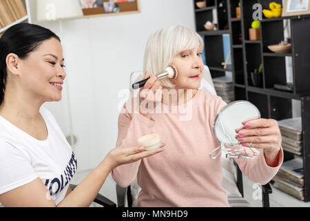 Jolly mature woman applying face powder Stock Photo