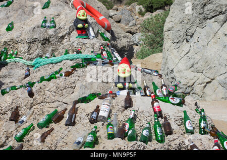 The beach of Tsampika, Rhodes island, Greece - September 21, 2017: Two figures of gnomes among beautifully laid out empty beer bottles on a huge bould Stock Photo