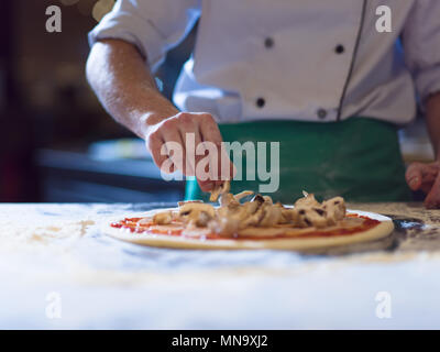 chef putting fresh mushrooms over pizza dough on kitchen table Stock Photo