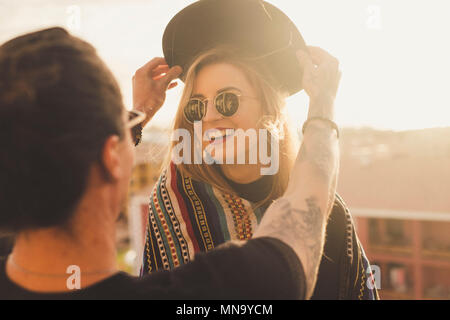 outdoor activity for couple of man and blonde young beautiful woman having fun together. he puts a hat on her head and she smile. sunlight and rooftop Stock Photo