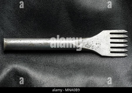 Leather punch tool. Tool for making holes in leather. Artificial leather background. Stock Photo
