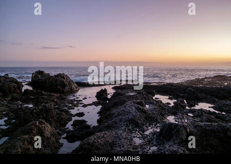 Sun setting over the black volcanic rocks and rock pools on the Tenerife coast with the waves of the Atlantic Ocean Stock Photo