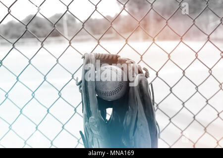 Old used ball in glove, view from team dugout.  Baseball field in background. Blue and orange on black and white. Stock Photo