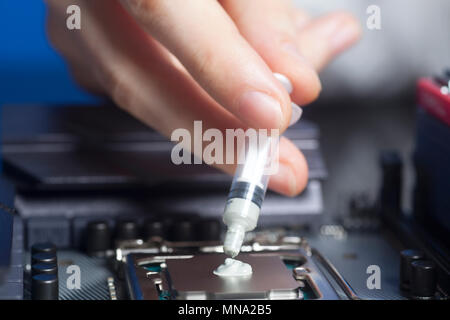 Hand with syringe applying thermal paste on the CPU processor on motherboard Close up Stock Photo