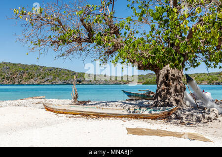 Traditional Rotenese fisherman's wooden boat laying under the tree near the water and fishing nets drying on the tree. Rote Island, Indonesia Stock Photo