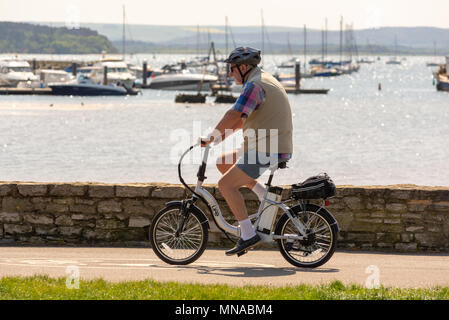 Senior gentleman wearing a helmet cycling along the Baiter Park seafront cycle path and past the marina, Poole, Dorset, UK Stock Photo