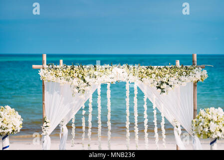 The beautiful wedding venue setting with white and green flowers, floral decoration on bamboo arch with panoramic ocean view in background Stock Photo