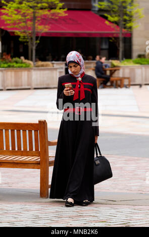 A Turkish Muslim woman wearing a black and red Abaya dress texting messages on her iPhone in Dundee city centre, UK Stock Photo