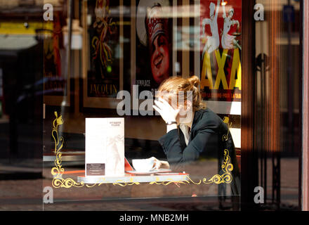 A young blonde woman sitting inside the Cordially Cake Cafe using her laptop and enjoying a cup of coffee in Dundee city centre, UK Stock Photo