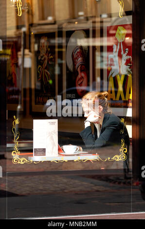 A young blonde woman sitting inside the Cordially Cake Cafe using her laptop and enjoying a cup of coffee in Dundee city centre, UK Stock Photo