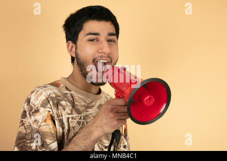 Young Man shouting in speaker on beige background Stock Photo
