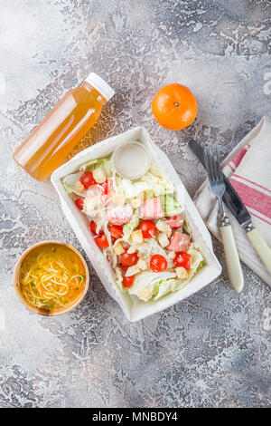 Caesar salad with salmon, cherry tomatoes, parmesan, lettuce, Chicken noodle soup in paper box, cutlery and bottle of green tea. Healthy food and diet Stock Photo