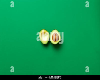 Avocado sliced with seed isolated in green background viewed from above - flatlay look Stock Photo