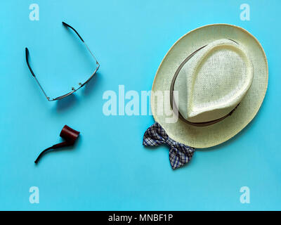 Pipe and glasses lying near straw hat and bow tie on blue background Stock Photo