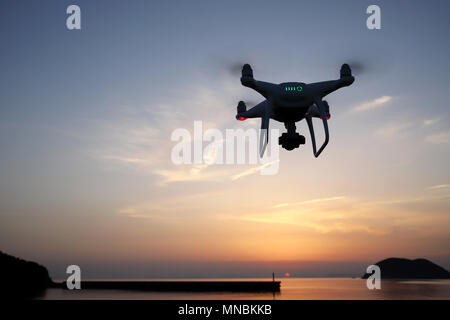 Remote controlled drone equipped with high resolution video camera flying above the sea against a sunset sky Stock Photo