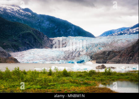 Mendenhall Glaier under cloudy skies in Tongass National Forest in Alaska. Proglacial lake with chunks of ice floating on it's surface forms at the gl Stock Photo