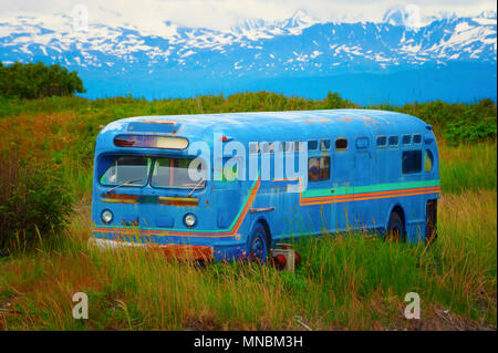 Kenai Mountain range is the backdrop of this old abandoned bus in a grassy field seen from walking path in Homer, Alaska. Stock Photo