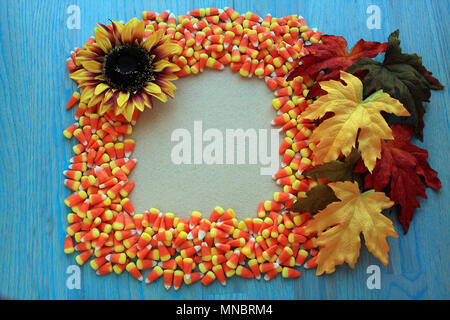 Candy corns inside the shape of a frame with a blank inside tan colored. With fall leaves and  sunflower around  outside. On rustic wooden background. Stock Photo