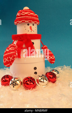 Snowman in snow with bells and with out. He has on gloves hat and scarf on a blue background. Snow around snowman. Vertical formats Photograph studios Stock Photo