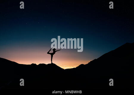 Fit Man in silhouette doing yoga natarajasana pose at night city and starry sky background Stock Photo