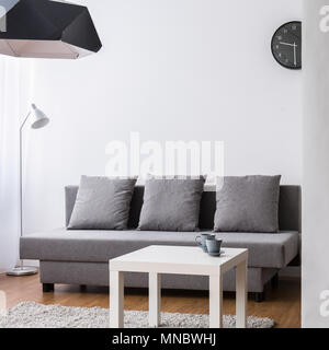 Modern living room with large, grey sofa and small coffee table. Light interior with decorative wallpaper. Stock Photo