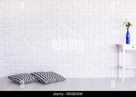 Decorative, black and white pattern pillows and small table standing in white interior with brick wall design Stock Photo