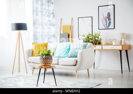 Stool with plant on grey carpet in cozy living room with cabinet and colorful pillows on couch next to a lamp Stock Photo