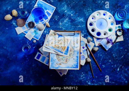 Artist workplace with a watercolor map, sketches, seashells and compass on a navy blue background with copy space. Travel flat lay header. Stock Photo