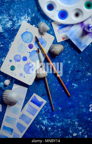 Creative artist workplace with marine watercolor, palettes, swatches, brushes and water jars from above. Painting sea concept on a navy blue backgroun Stock Photo