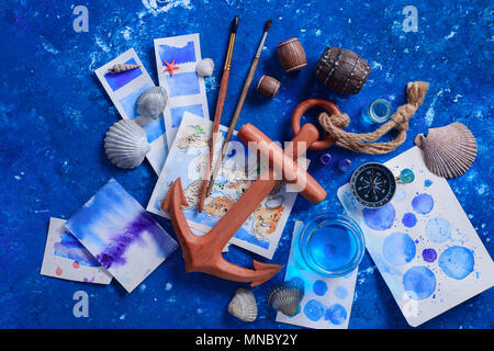 Artist workplace with watercolor sketches, seashells, wooden anchor and compass on a navy blue background with copy space. Creative travel and paintin Stock Photo